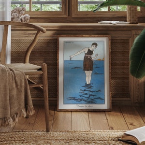 May include: A framed vintage illustration of a woman in a swimsuit standing in the ocean. The illustration is in a wooden frame and is hanging on a wall. The wall is made of wood and has a woven rattan panel.