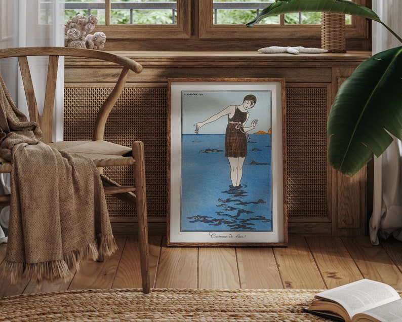 May include: A framed vintage illustration of a woman in a swimsuit standing in the ocean. The illustration is in a wooden frame and is hanging on a wall. The wall is made of wood and has a woven rattan panel.