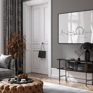 May include: A black and white line drawing of the London skyline, including the London Eye, Big Ben, and Tower Bridge, is framed and hanging on a gray wall. A black console table with two shelves holds books and a black lamp with a marble shade.