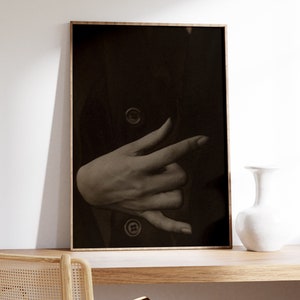 Op de afbeelding: Een zwart-witfoto van een hand die een gebaar maakt, ingelijst in een houten lijst.
