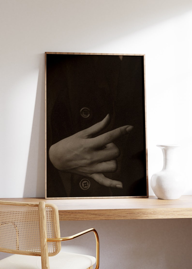 Op de afbeelding: Een zwart-witfoto van een hand die een gebaar maakt, ingelijst in een houten lijst.