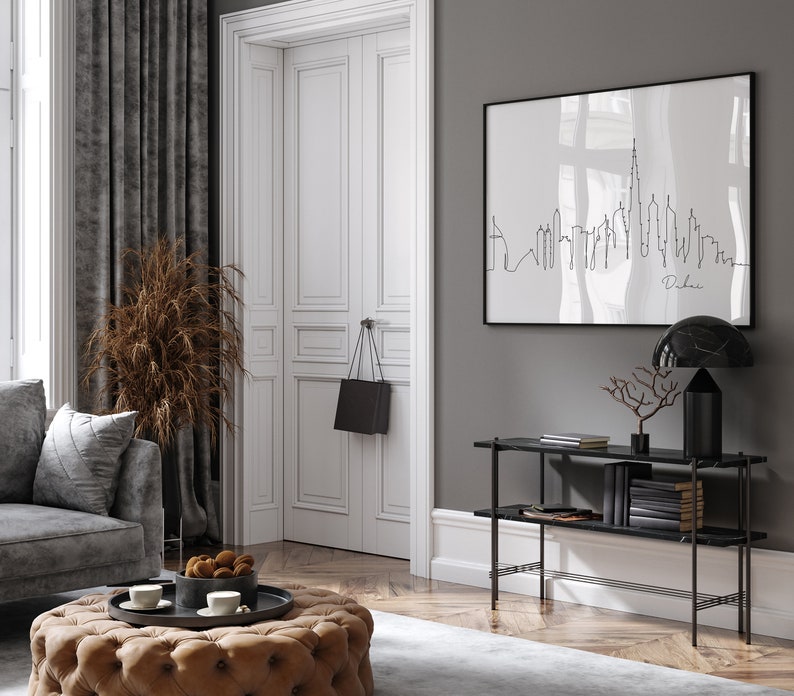 May include: A black and white line art print of the Dubai skyline hanging on a gray wall above a black console table with two shelves. The table has a black marble top and a black metal frame. A black lamp with a marble shade sits on the table.