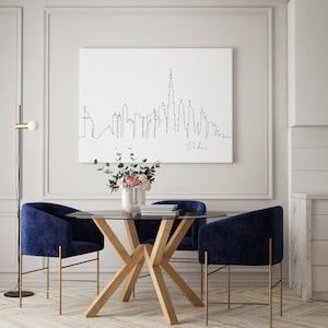 May include: A dining room with a glass-top table and four blue velvet chairs. The table has a wooden base with a unique X-shaped design. A black floor lamp with a white globe is in the corner of the room. A framed print of a line drawing of the Dubai skyline hangs on the wall.