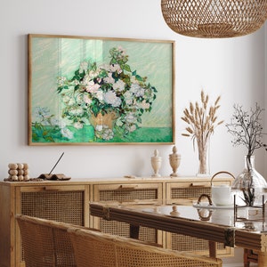 K&ouml;nnte beinhalten: Ein gerahmtes Gem&auml;lde eines wei&szlig;en Blumenstrau&szlig;es in einer Vase vor gr&uuml;nem Hintergrund. Das Gem&auml;lde h&auml;ngt an einer wei&szlig;en Wand &uuml;ber einem Holzschrank mit einer geflochtenen Rattanfront.