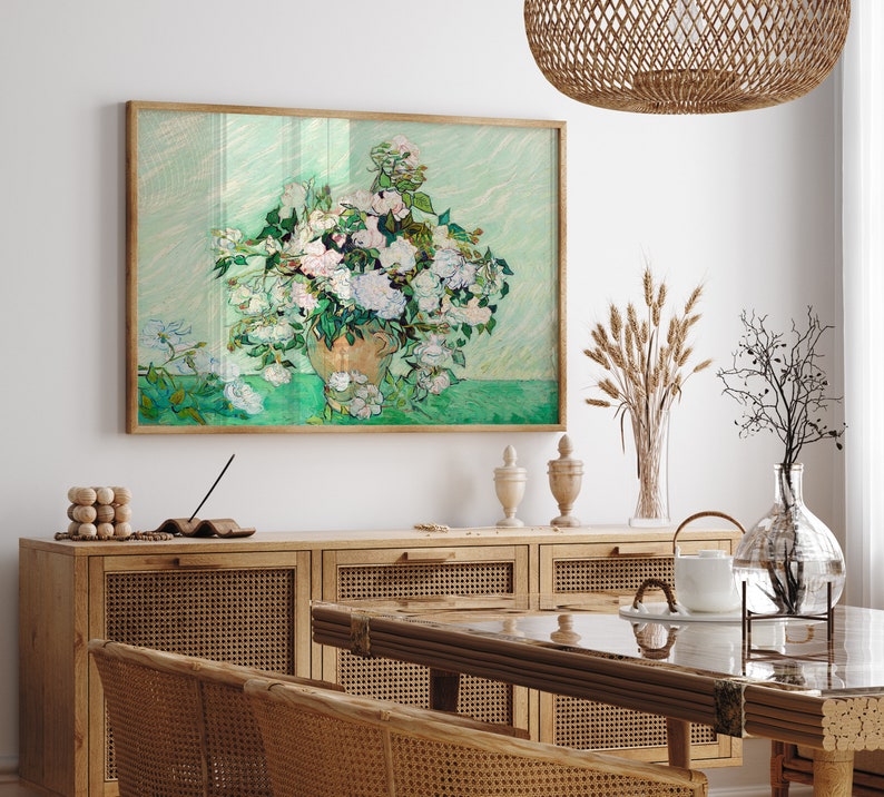 K&ouml;nnte beinhalten: Ein gerahmtes Gem&auml;lde eines wei&szlig;en Blumenstrau&szlig;es in einer Vase vor gr&uuml;nem Hintergrund. Das Gem&auml;lde h&auml;ngt an einer wei&szlig;en Wand &uuml;ber einem Holzschrank mit einer geflochtenen Rattanfront.