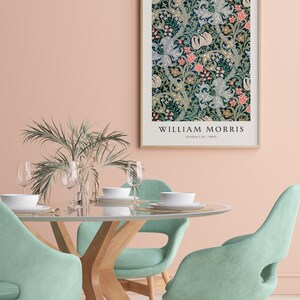 May include: A framed print of a floral pattern by William Morris, titled "Golden Lily" from 1880. The print is hanging on a pale pink wall above a dining table with four light green chairs.