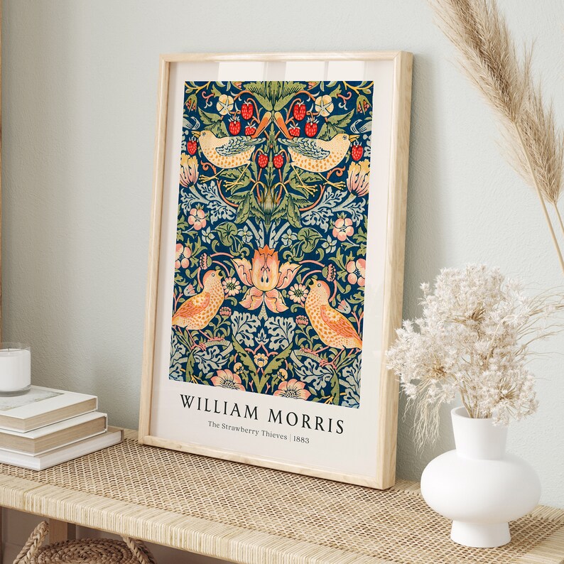 Op de afbeelding: Een ingelijste print van een vintage botanische illustratie van William Morris, met een herhalend patroon van vogels, bloemen en bladeren op een donkerblauwe achtergrond. De titel "The Strawberry Thieves" en het jaar "1883" zijn onder de afbeelding gedrukt.