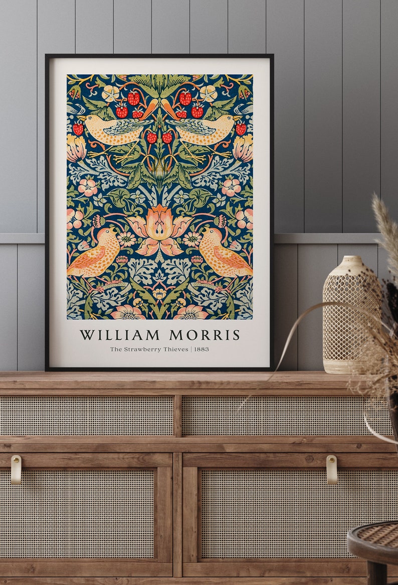 Op de afbeelding: Een ingelijste print van een vintage ontwerp van William Morris met een blauwe achtergrond met een bloemenpatroon en twee vogels. De tekst "William Morris" staat onderaan de print, samen met de titel "The Strawberry Thieves" en het jaar "1883".