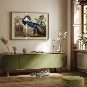 K&ouml;nnte beinhalten: Ein gr&uuml;ner Schrank mit drei T&uuml;ren steht auf einem Holzboden. Ein gerahmtes Bild eines blauen Vogels mit langem Hals und langen Beinen h&auml;ngt an der Wand &uuml;ber dem Schrank. Eine kleine Topfpflanze steht auf dem Schrank neben einem Buch. Eine kleine Topfpflanze und eine Vase mit Blumen stehen auf dem Boden neben dem Schrank.