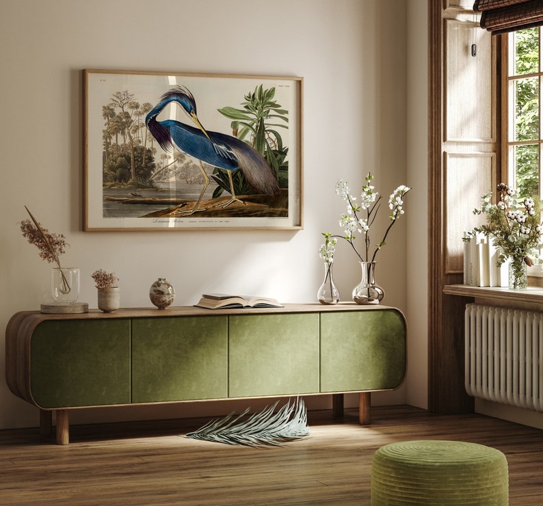 K&ouml;nnte beinhalten: Ein gr&uuml;ner Schrank mit drei T&uuml;ren steht auf einem Holzboden. Ein gerahmtes Bild eines blauen Vogels mit langem Hals und langen Beinen h&auml;ngt an der Wand &uuml;ber dem Schrank. Eine kleine Topfpflanze steht auf dem Schrank neben einem Buch. Eine kleine Topfpflanze und eine Vase mit Blumen stehen auf dem Boden neben dem Schrank.