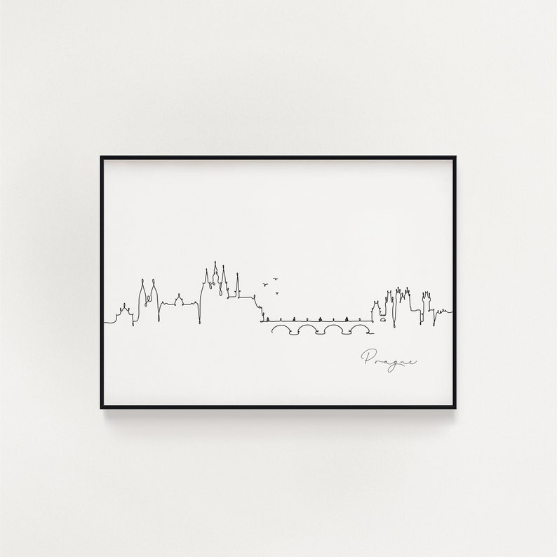 May include: A black framed art print with a minimalist line drawing of the Prague skyline. The artwork includes the Charles Bridge and the word "Prague" in cursive. The print is on a white background.