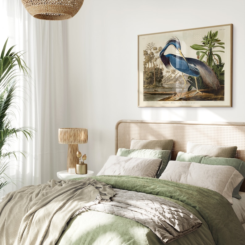 K&ouml;nnte beinhalten: Ein gr&uuml;nes und beiges Schlafzimmer mit einem Bett, das mit einer gr&uuml;nen Bettdecke und einer grauen Wolldecke ausgestattet ist. Ein gerahmtes Bild eines blauen Reihers h&auml;ngt an der Wand &uuml;ber dem Bett. Ein Kopfteil aus Weidengeflecht und eine Weidenlampe sind ebenfalls zu sehen.
