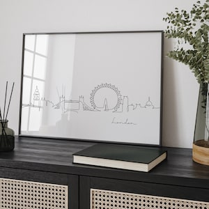 May include: Black and white line art print of the London skyline, including the London Eye, Big Ben, and Tower Bridge. The print is framed in a black frame and is hanging on a wall above a black cabinet with woven cane doors.