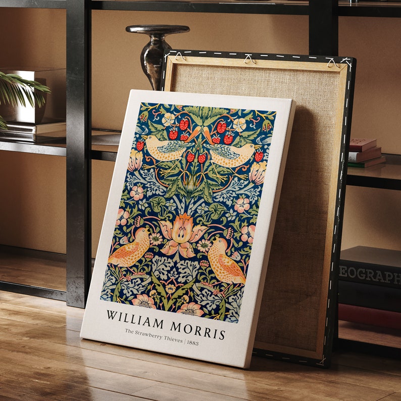 Op de afbeelding: Een canvas print van William Morris' ontwerp "The Strawberry Thieves". De print heeft een blauwe achtergrond met een herhalend patroon van vogels, bloemen en bladeren. De tekst "William Morris" en "The Strawberry Thieves | 1883" staat onderaan de print.