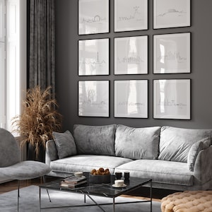 May include: A living room with a gray sofa, a coffee table, and a gray armchair. The wall is decorated with nine black framed prints of city skylines. The prints are arranged in a grid pattern.