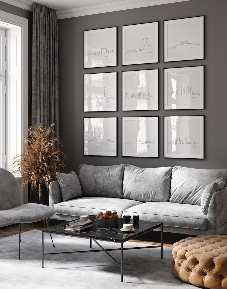 May include: A living room with a gray sofa, a coffee table, and a gray armchair. The wall is decorated with nine black framed prints of city skylines. The prints are arranged in a grid pattern.