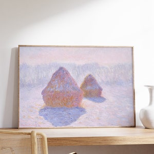 May include: A framed painting depicting a winter scene with two haystacks in the foreground. The haystacks are painted in shades of pink, purple, and yellow, with a soft, hazy blue background. The painting is signed "Claude Monet 91" in the bottom left corner.