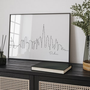May include: Black and white line art print of the Dubai skyline in a black frame. The print is on a white background and the word "Dubai" is written in cursive below the skyline.