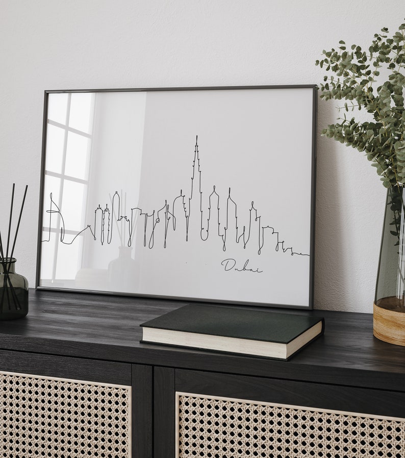 May include: Black and white line art print of the Dubai skyline in a black frame. The print is on a white background and the word "Dubai" is written in cursive below the skyline.