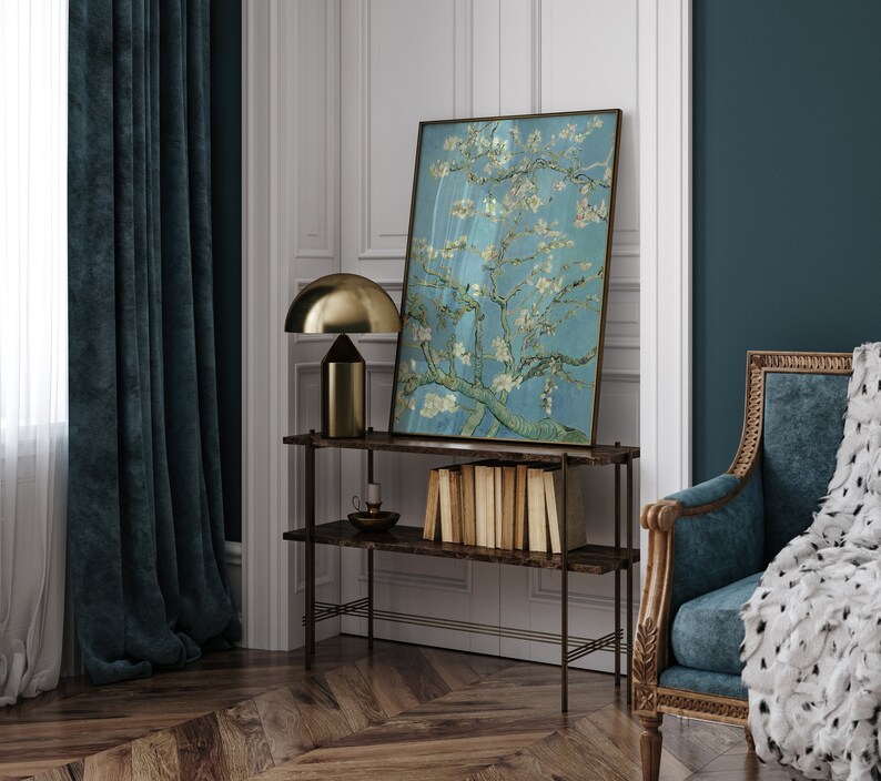Puede incluir: Una cortina de terciopelo azul oscuro cuelga frente a una ventana con cortinas blancas transparentes. Una l&aacute;mpara de mesa dorada con una pantalla en forma de hongo se encuentra sobre un estante de madera oscura con una pintura de un almendro en flor en un esquema de color azul claro y blanco. El estante forma parte de una unidad de estanter&iacute;a de marco de metal negro. Un sill&oacute;n de terciopelo azul oscuro con una manta de piel sint&eacute;tica blanca se encuentra en la esquina de la habitaci&oacute;n.