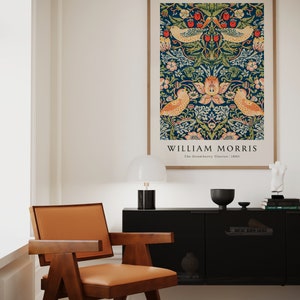 Op de afbeelding: Een ingelijste print van een vintage William Morris-ontwerp met een herhalend patroon van vogels, bloemen en bladeren op een donkerblauwe achtergrond. De tekst "William Morris" en "The Strawberry Thieves 1883" is onder het ontwerp gedrukt.