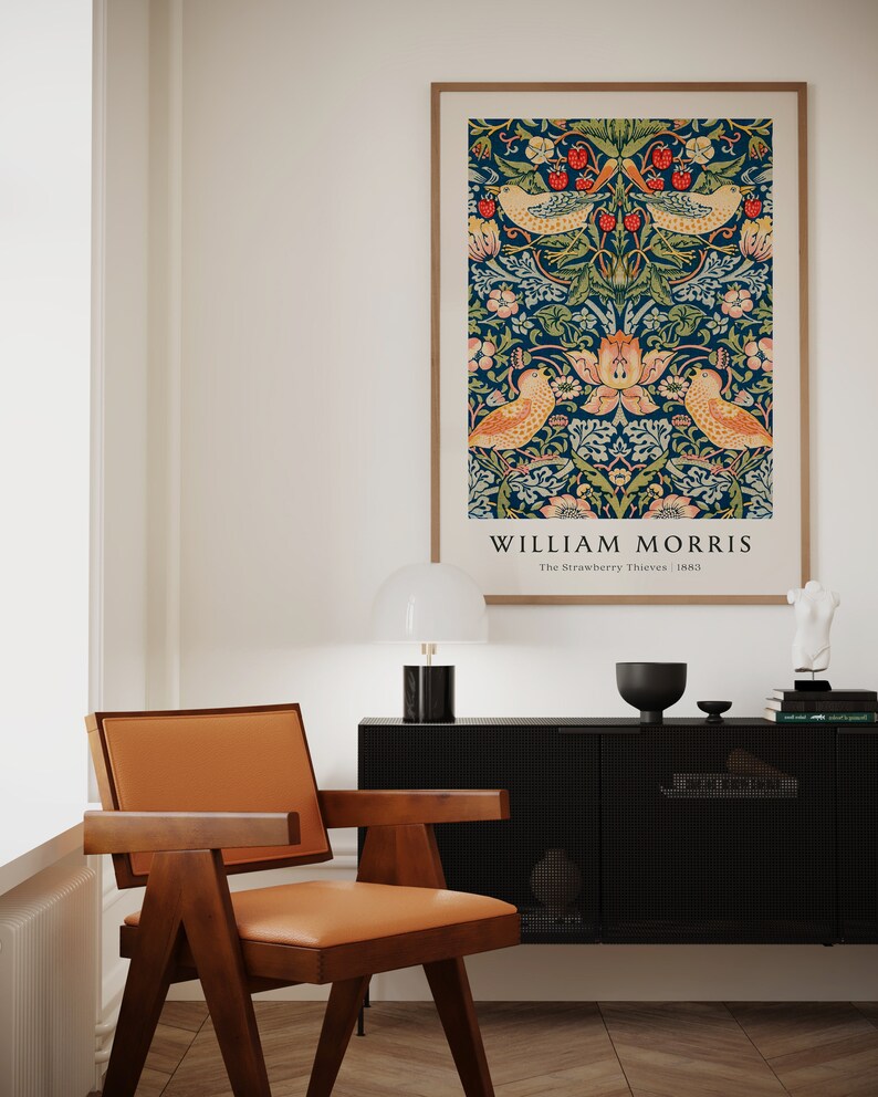 Op de afbeelding: Een ingelijste print van een vintage William Morris-ontwerp met een herhalend patroon van vogels, bloemen en bladeren op een donkerblauwe achtergrond. De tekst "William Morris" en "The Strawberry Thieves 1883" is onder het ontwerp gedrukt.