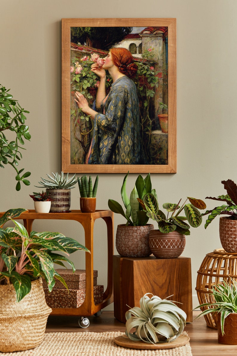 Op de afbeelding: Een ingelijst schilderij van een vrouw in een blauwe en gouden jurk die aan een roze roos ruikt in een tuin. Het schilderij is omringd door planten in potten, waaronder een slangplant, een succulent en een spinplant.