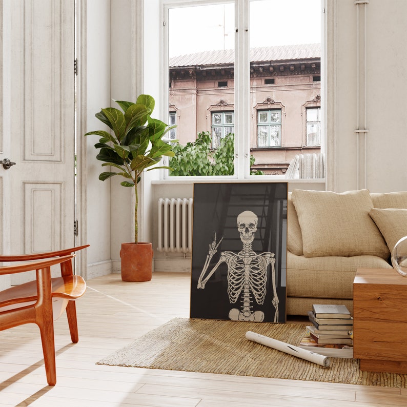 May include: A black and white poster featuring a skeleton with a peace sign. The poster is hanging on a wall in a living room with a couch, a plant, and a chair.