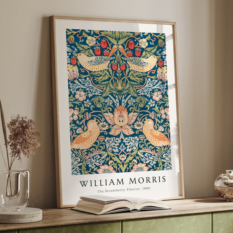 Op de afbeelding: Een ingelijste print van een vintage William Morris-ontwerp met een herhalend patroon van vogels, bloemen en bladeren in tinten blauw, groen, roze en geel. De tekst "William Morris The Strawberry Thieves | 1883" is onder het ontwerp gedrukt.