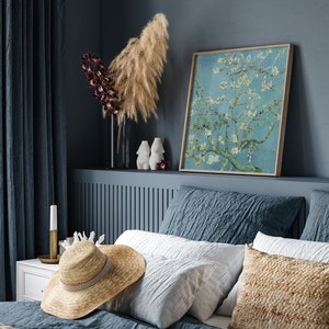 Puede incluir: Un dormitorio con una cabecera azul y una cama con ropa de cama blanca y azul. Un sombrero de paja est&aacute; en la cama. Una impresi&oacute;n enmarcada de una pintura de un &aacute;rbol en flor est&aacute; en la pared sobre la cabecera.