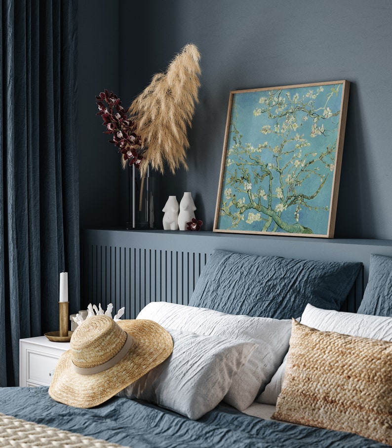 Puede incluir: Un dormitorio con una cabecera azul y una cama con ropa de cama blanca y azul. Un sombrero de paja est&aacute; en la cama. Una impresi&oacute;n enmarcada de una pintura de un &aacute;rbol en flor est&aacute; en la pared sobre la cabecera.
