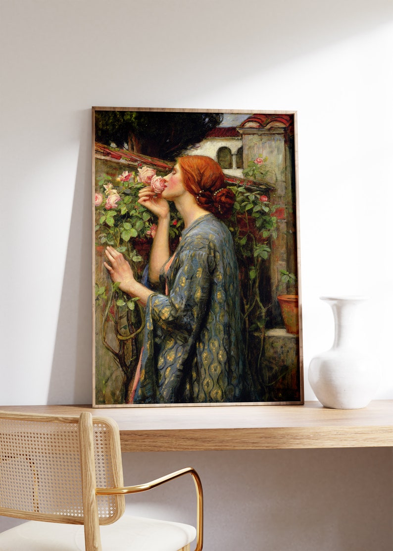 Op de afbeelding: Een schilderij van een vrouw in een blauwe en gouden gebloemde jurk, die aan een roze rozenstruik ruikt. De vrouw heeft rood haar en staat in een tuin.