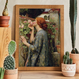 Op de afbeelding: Een ingelijst schilderij van een vrouw in een blauwe en gouden jurk die aan een roze roos ruikt. De vrouw staat in een tuin met een stenen muur en een gebouw op de achtergrond.