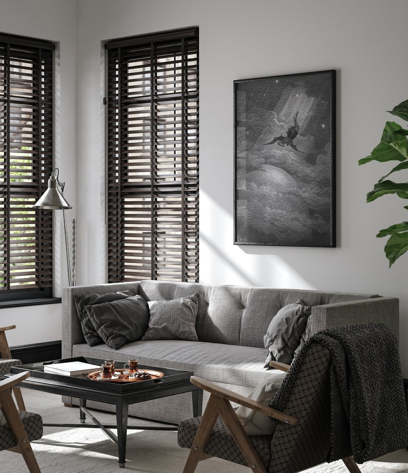 May include: A gray sofa with dark gray pillows sits in a living room with a black coffee table and a framed black and white print of a winged figure flying through the clouds. The room has brown wood blinds on the windows and a wooden chair with a black and white patterned throw blanket.