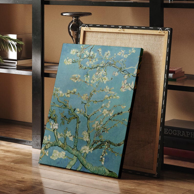Puede incluir: Una impresi&oacute;n en lienzo de una pintura que representa un almendro en flor con flores blancas sobre un fondo de cielo azul. La pintura est&aacute; enmarcada y apoyada en un estante de madera.