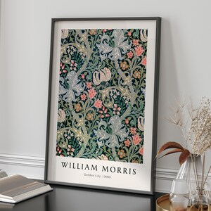 May include: A framed print of a vintage floral pattern in shades of green, blue, pink, and yellow. The print features a repeating design of stylised flowers and leaves. The text "WILLIAM MORRIS" and "Golden Lily | 1880" is printed below the image.