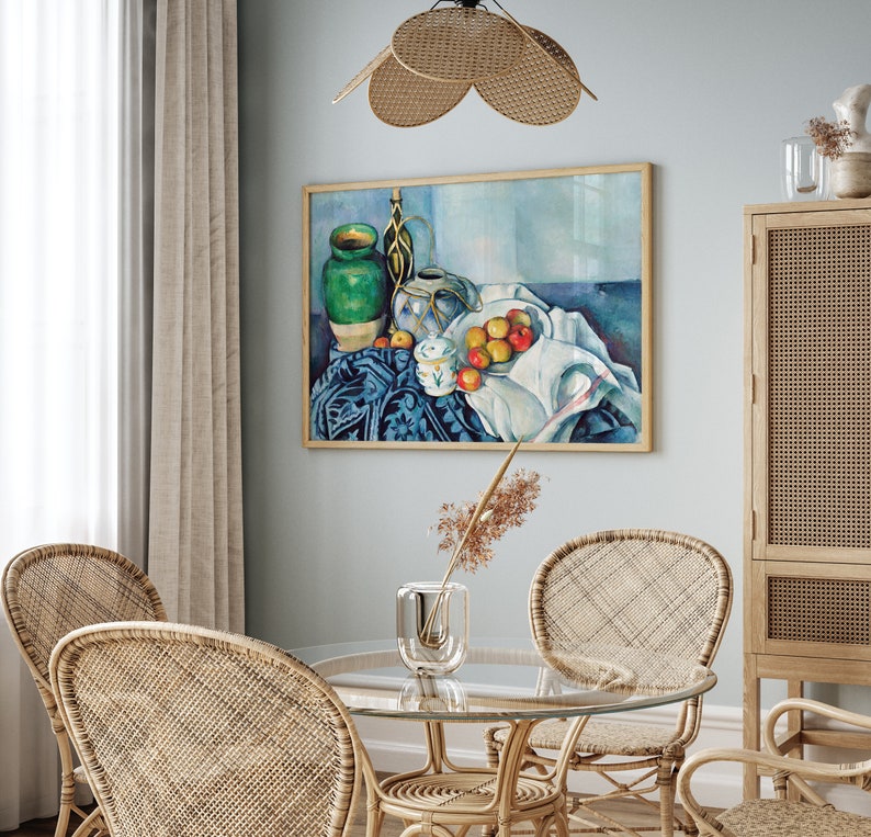 May include: A still life painting of a green ceramic vase, a white ceramic pitcher, and a bowl of red apples on a blue and white tablecloth. The painting is framed and hanging on a light blue wall.