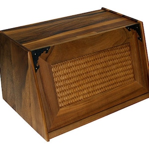 May include: A wooden bread box with a woven wicker front panel and black metal hinges. The box has a slanted lid and a dark wood finish.