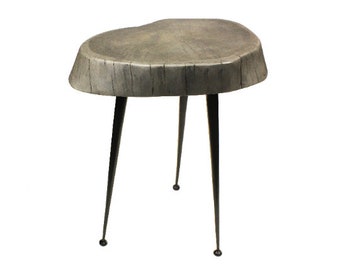 May include: A gray wooden side table with a unique, irregular shape and three black metal legs.