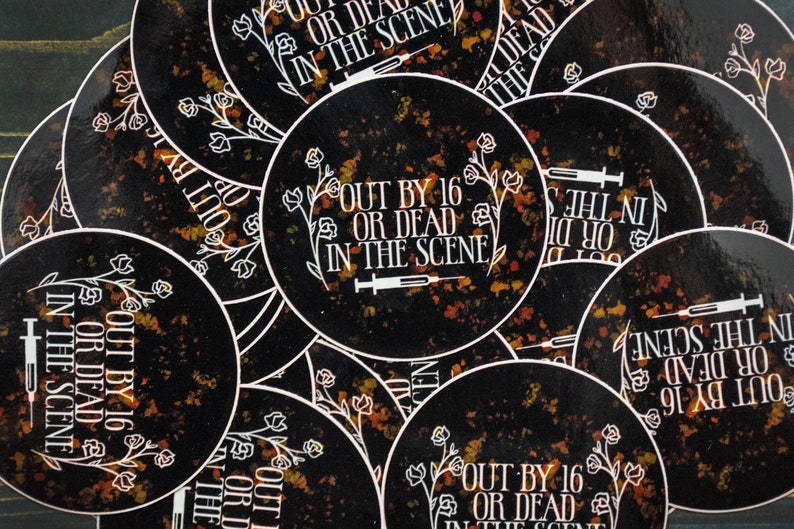 May include: A stack of black and orange round stickers with the text "Out by 16 or dead in the scene" and a syringe graphic.