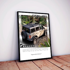 Puede incluir: Un póster enmarcado con un SUV de color claro, el Bronco Everglades, en un sendero embarrado. El póster incluye el texto "EVERGLADES" y "BRONCO", junto con el lema: "Engineered for Adventure."