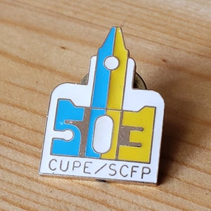 May include: A silver pin with a white, yellow, and blue design. The pin features a stylized pen and the number 50. The text "CUPE/SCFP" is printed below the design.