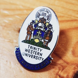 May include: A silver pin with a white background and blue and gold accents. The pin features the Trinity Western University logo and the text "25th Anniversary".