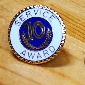 May include: A gold-coloured pin with a white and blue circle. The circle says "SERVICE 10 AWARD" in a white circle with a blue background. The number 10 is in a gold circle.
