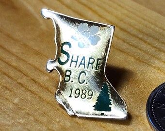 May include: Gold-colored pin shaped like the outline of British Columbia with the text "Share B.C. 1989" and a small green tree. The pin is next to a Canadian quarter.
