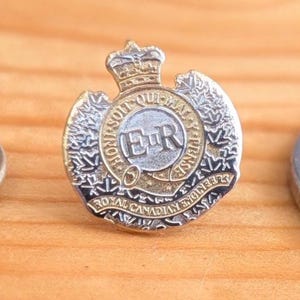 May include: A circular Royal Canadian Engineers badge with a crown, the initials "ER", and the words "Royal Canadian Engineers" and "Dieu et mon droit". The badge is gold, silver, and black.