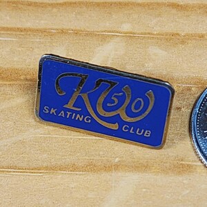 May include: A blue and gold pin with the text "R50 Skating Club" in a cursive font.