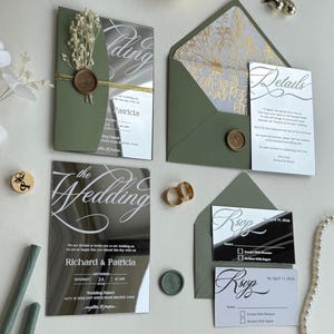 Può includere: Elegante suite di inviti di nozze con biglietti a specchio, calligrafia e buste verde oliva. Include biglietti RSVP, biglietto dei dettagli e un sigillo di cera. L'invito recita "The Wedding".