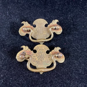 Puede incluir: Dos tiradores de armario de latón antiguo con diseños florales ornamentados. Los tiradores tienen un asa de bucle y están en buen estado.