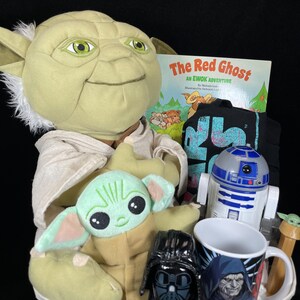 Op de afbeelding: Een Star Wars-thema cadeaupakket gevuld met een Yoda-knuffel, een Baby Yoda-knuffel, een Darth Vader-beeldje, een R2-D2-speelgoed, een mok met een karakterprint, een kinderboek getiteld "The Red Ghost" en een zwart t-shirt.